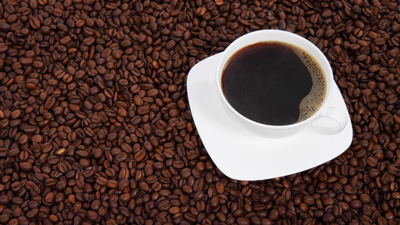 Grãos de café torrados ao lado de uma xícara fumegante.