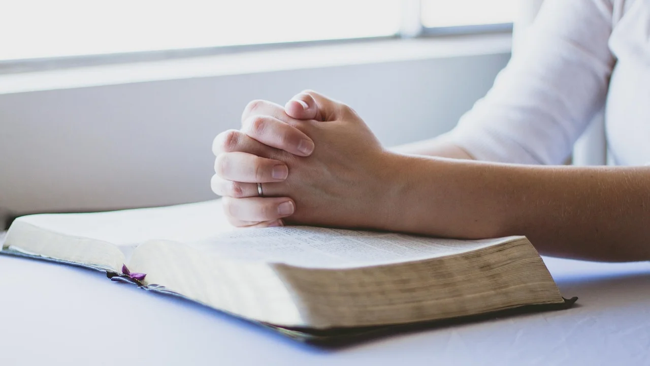 Mãos unidas em gesto de oração diante da luz do amanhecer.