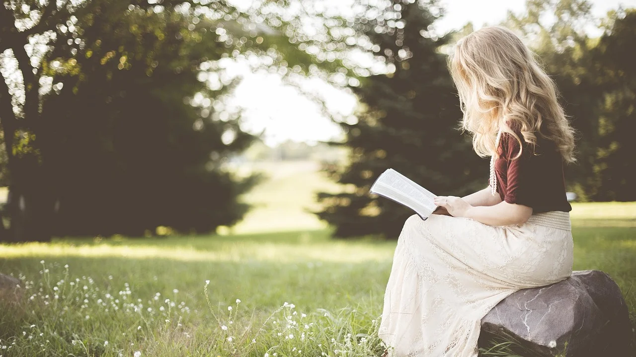 Criança acompanha a leitura de um livro com apoio de um adulto.