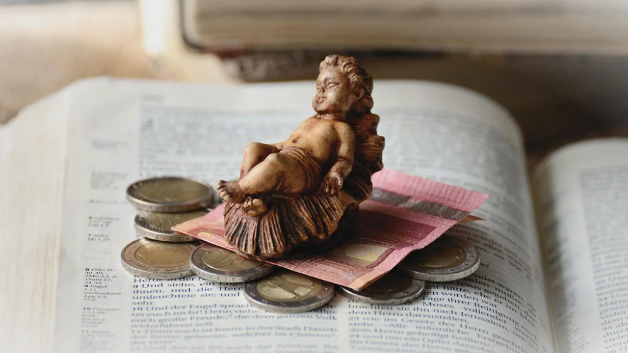 Bíblia aberta ao lado de moedas sobre uma mesa de madeira.